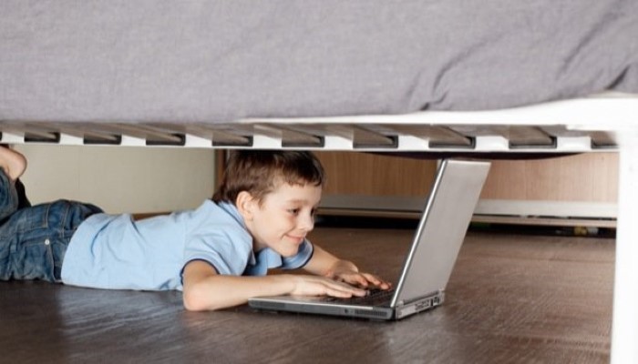 Enfant caché sous le lit avec un ordinateur Enfant caché sous le lit avec un ordinateur