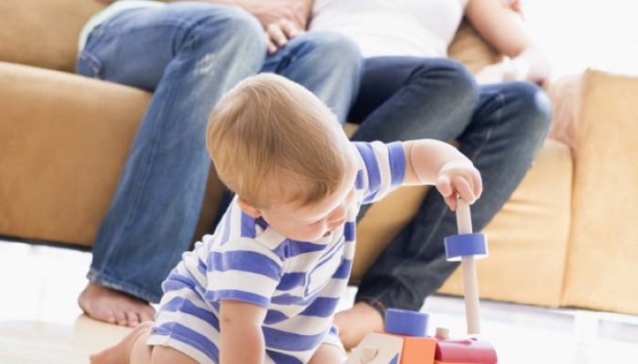 Bébé qui joue dans le salon avec ses parents assis sur le canapé Bébé qui joue dans le salon avec ses parents assis sur le canapé
