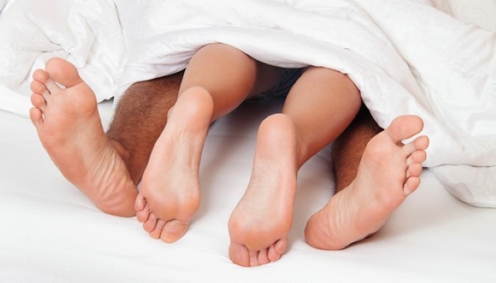 Jambes d'un couple qui dépassent de sous la couette