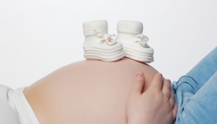 Femme enceinte avec des petits chaussons posés sur le ventre