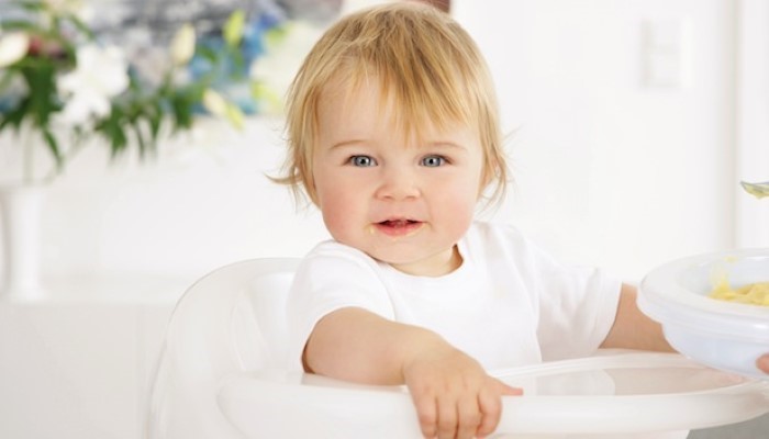Bébé assis dans une chaise-haute qui sourit Bébé assis dans une chaise-haute qui sourit
