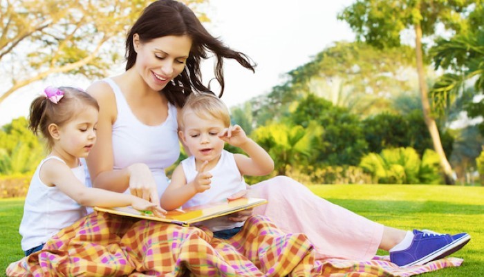 Maman avec ses deux enfants lisent un livre à l'air libre
