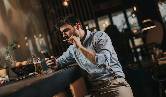 Homme qui boit une bière en fumant une cigarette